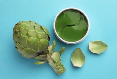 Photo of Package of under eye patches and artichoke on light blue background, flat lay. Cosmetic product