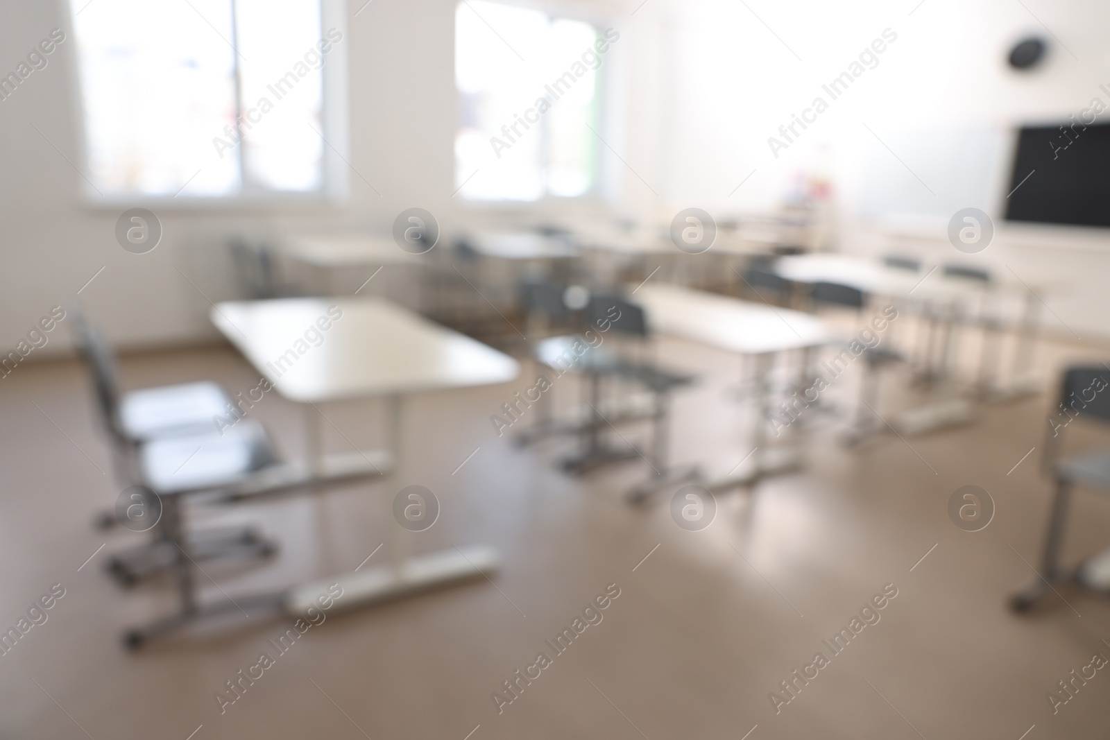 Photo of Blurred view of empty school classroom with desks, windows and chairs