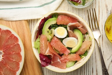 Photo of Delicious pomelo salad with prosciutto in half of fruit on white wooden table, flat lay
