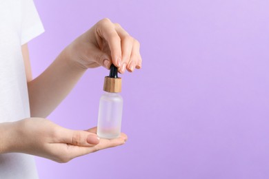 Photo of Woman holding bottle with serum against lilac background, closeup. Space for text
