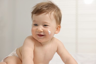 Cute little baby with moisturizing cream on face indoors