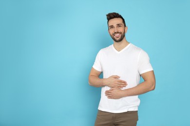 Photo of Happy man touching his belly on light blue background, space for text. Concept of healthy stomach
