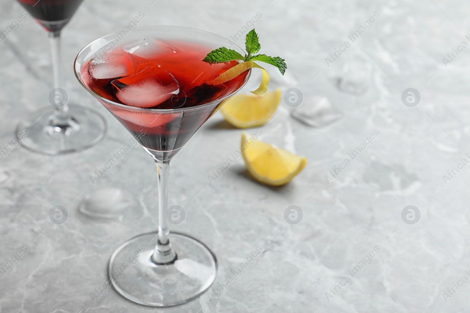 Photo of Glass of delicious cocktail with ice on light grey table. Space for text