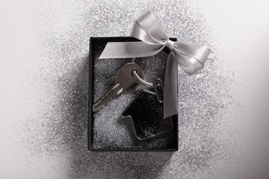 Photo of Key with trinket in shape of house, glitter and gift box on light grey background, top view. Housewarming party