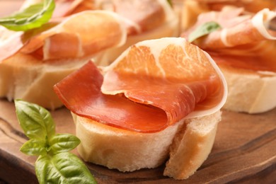 Tasty sandwiches with cured ham and basil leaves on wooden board, closeup