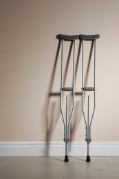 Photo of Pair of axillary crutches near beige wall. Space for text