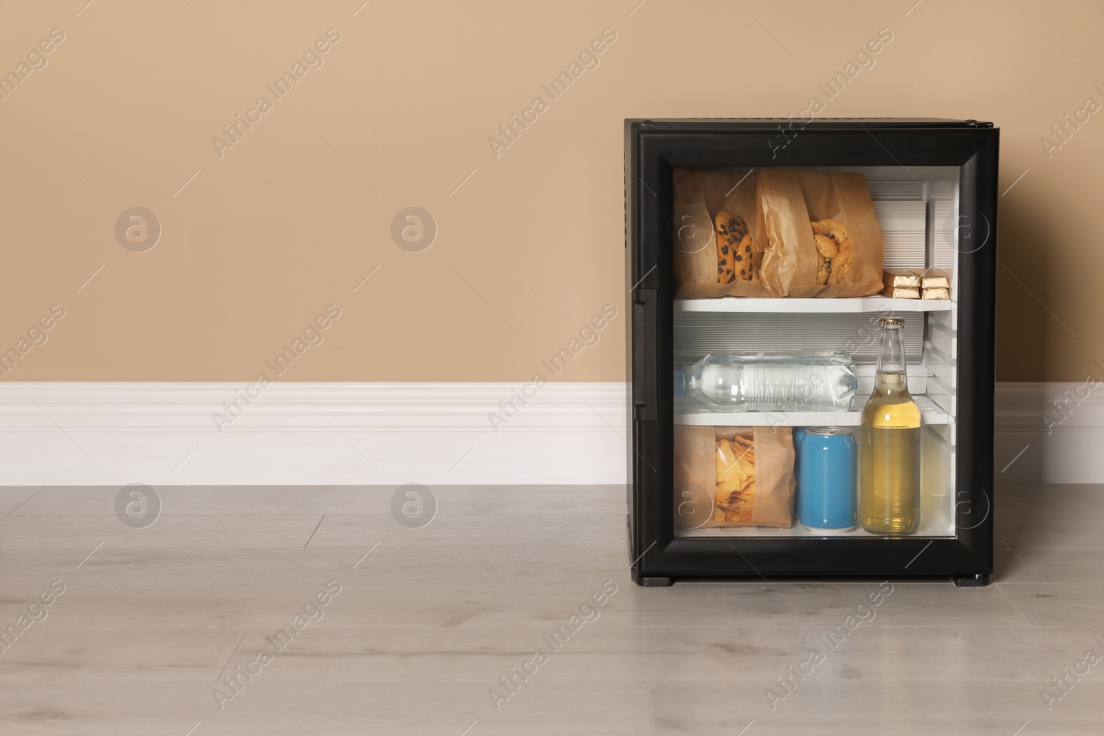 Photo of Mini bar filled with food and drinks near beige wall indoors, space for text