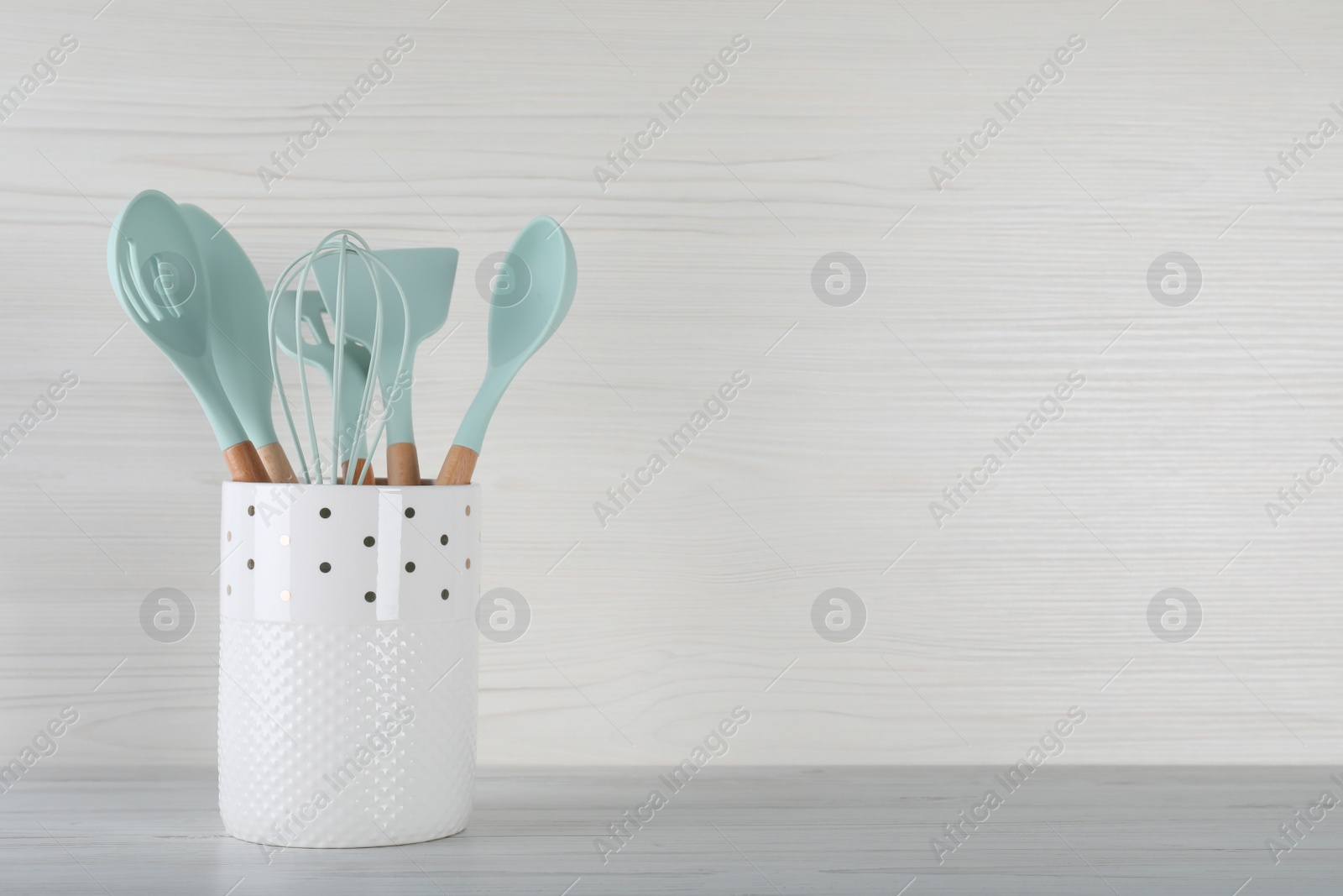 Photo of Holder with different kitchen utensils on white wooden table. Space for text