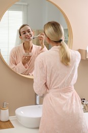 Photo of Woman applying face mask near mirror in bathroom. Spa treatments