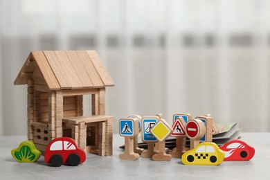 Set of wooden road signs, cars and house on light grey table indoors. Children's toys