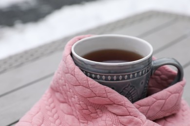 Photo of Winter morning. Cup with hot drink wrapped in pink sweater outdoors, closeup. Space for text