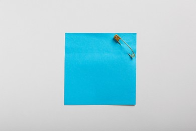 Photo of Blue paper note attached with safety pin on white background, top view