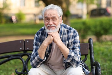 Portrait of happy grandpa with glasses on bench in park