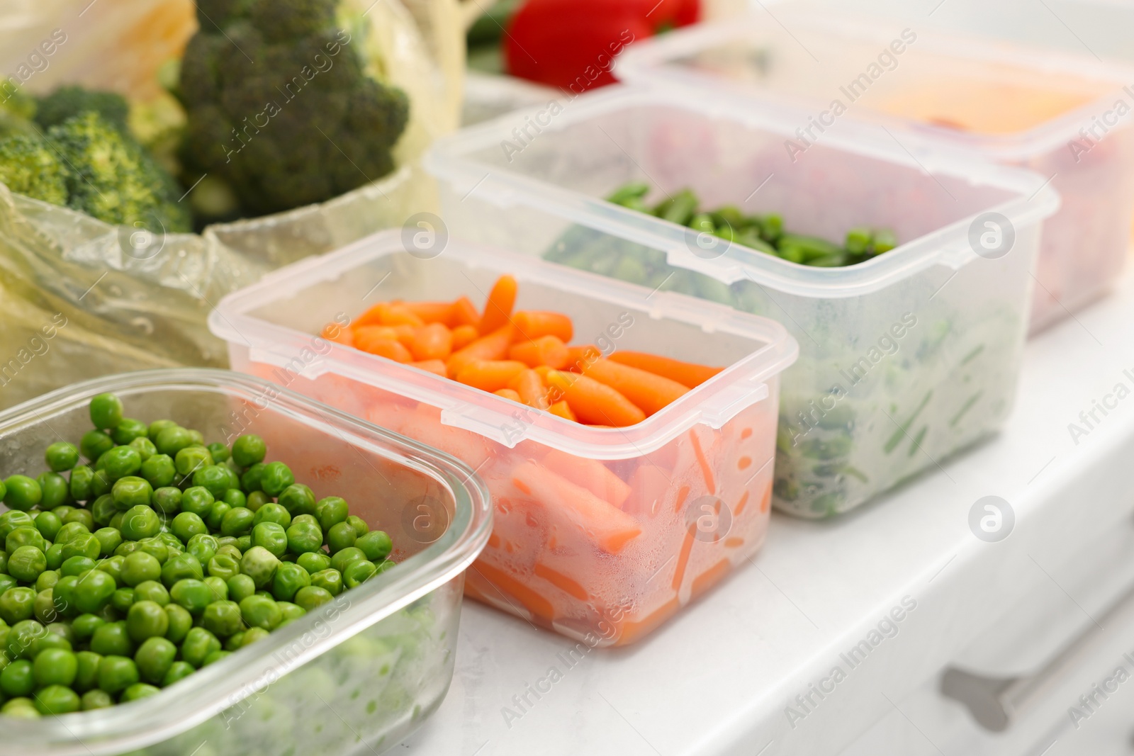 Photo of Plastic and glass containers with different fresh products on white countertop, closeup