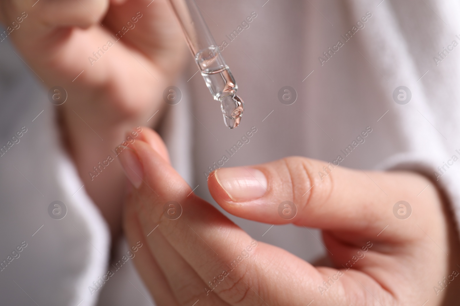 Photo of Woman applying cosmetic serum onto finger, closeup view