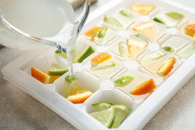 Pouring juice into ice cube tray with lime and orange on light table, closeup
