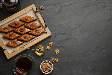 Photo of Delicious sweet baklava with walnuts, honey and hot tea on black table, flat lay. Space for text