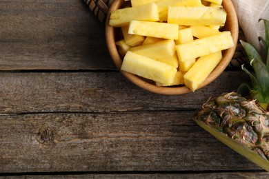 Photo of Pieces of tasty ripe pineapple in bowl on wooden table, flat lay. Space for text