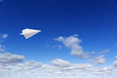 Image of White paper plane flying in blue sky with clouds