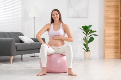 Pregnant woman sitting on fitness ball at home. Doing yoga