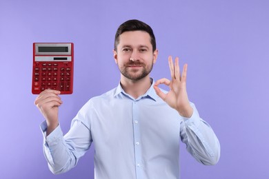 Photo of Happy accountant with calculator showing ok gesture on violet background