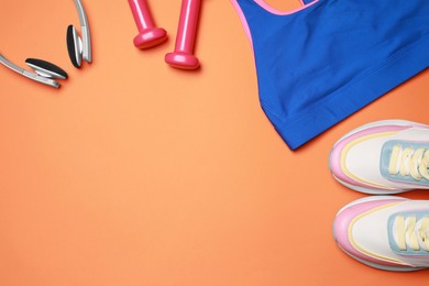 Photo of Stylish sportswear, dumbbells and headphones on orange background, flat lay. Space for text