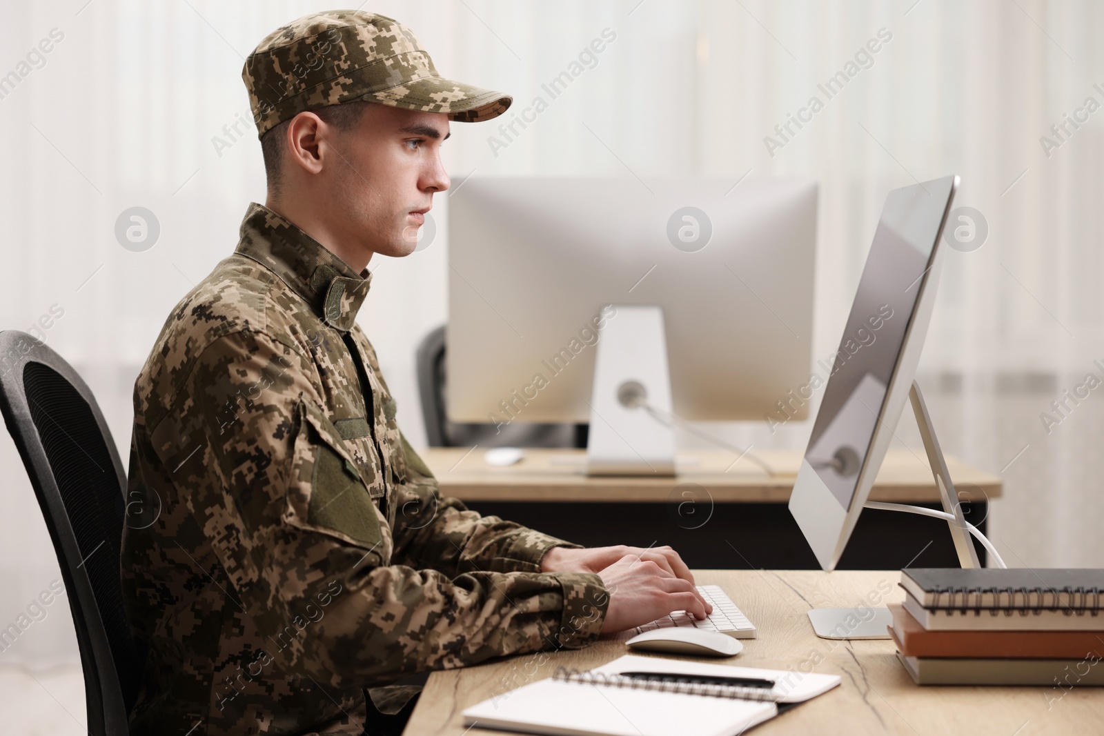 Photo of Military service. Young soldier working with computer at wooden table in office