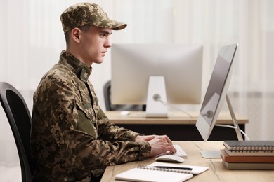Photo of Military service. Young soldier working with computer at wooden table in office