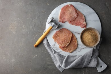 Photo of Cooking schnitzel. Raw pork chops, bread crumbs with meat mallet on grey table, top view and space for text