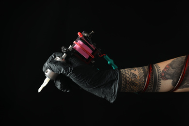Tattoo artist with professional machine on black background, closeup