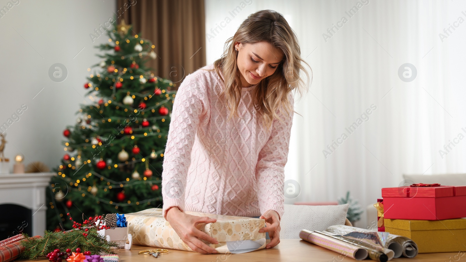 Photo of Beautiful young woman wrapping Christmas gift at home