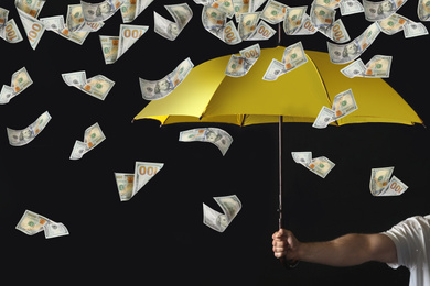 Man holding yellow umbrella under money rain on black background, closeup 