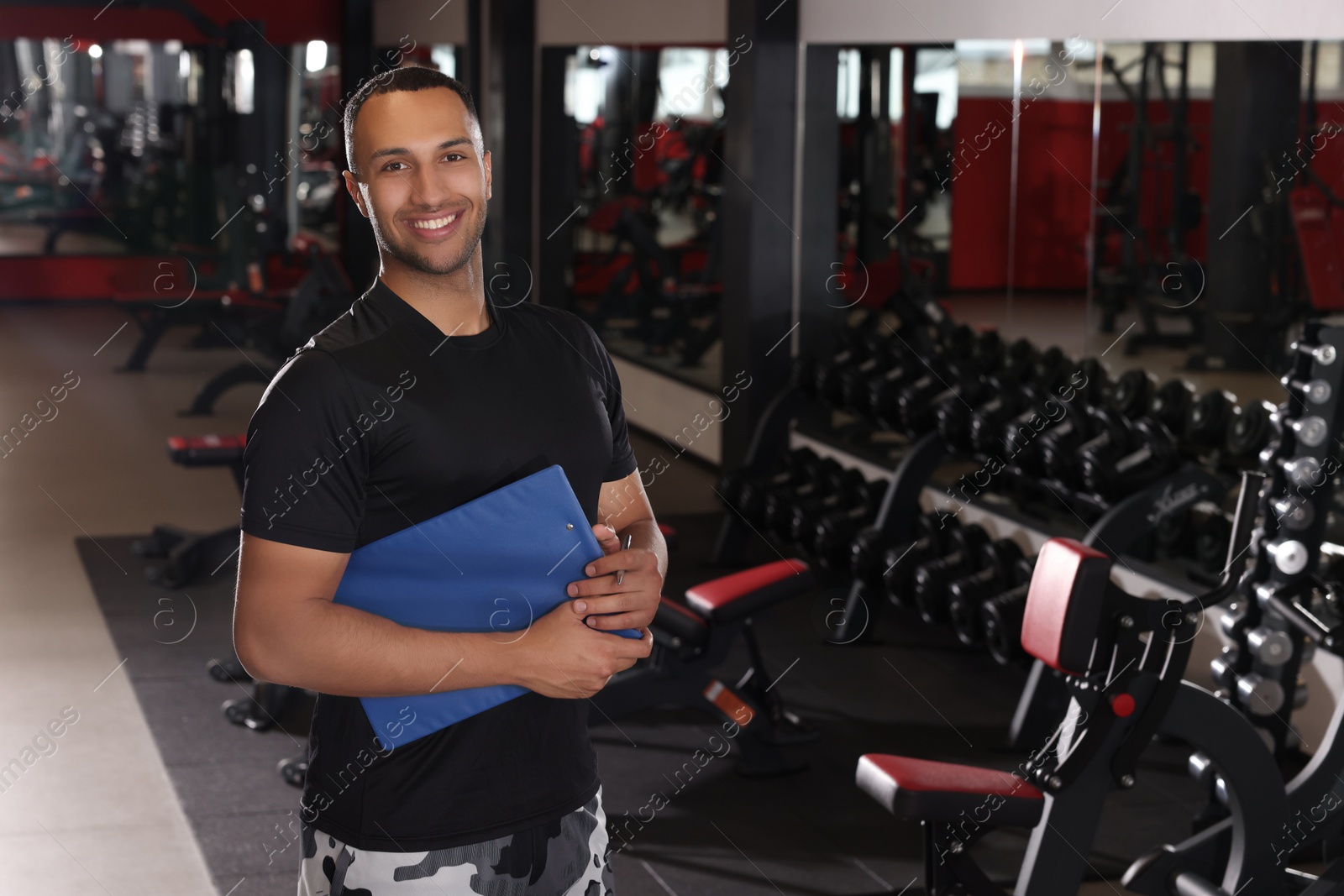 Photo of Happy trainer with workout plan in modern gym, space for text