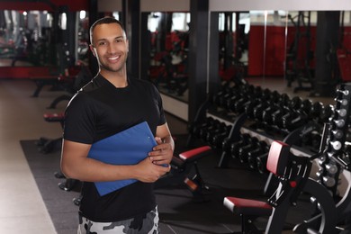 Happy trainer with workout plan in modern gym, space for text