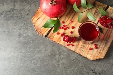 Photo of Board with glass of pomegranate juice and fresh fruits on grey background, top view. Space for text