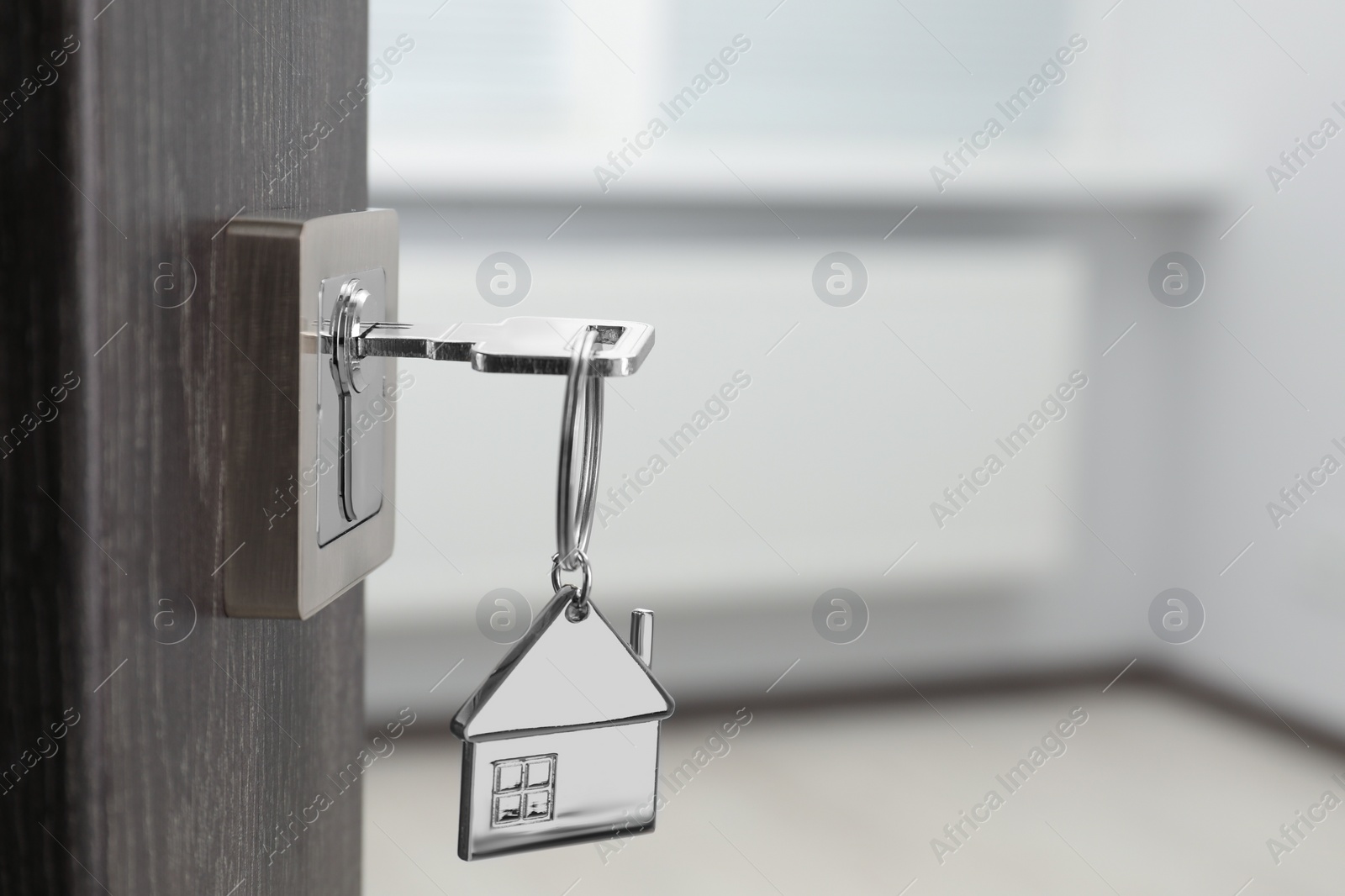 Photo of Mortgage and real estate. Open door with key and house shaped keychain against blurred background, space for text