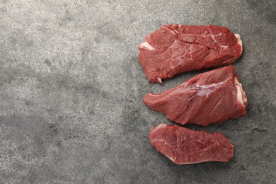 Pieces of raw beef meat on grey table, flat lay. Space for text