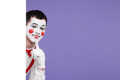 Funny mime artist peeking out of blank poster on purple background. Space for text