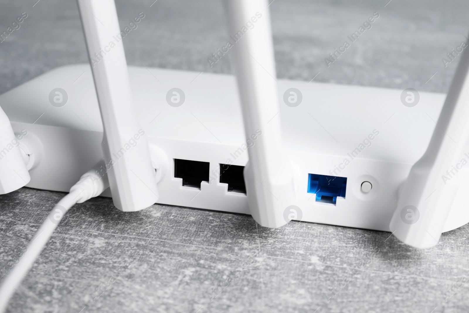 Photo of New white Wi-Fi router on grey textured table, closeup