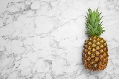 Photo of Whole ripe pineapple on white marble table, top view. Space for text