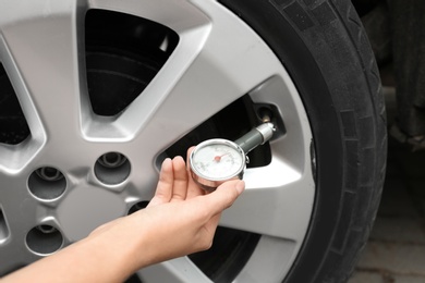 Photo of Woman checking car tire pressure with air gauge, closeup