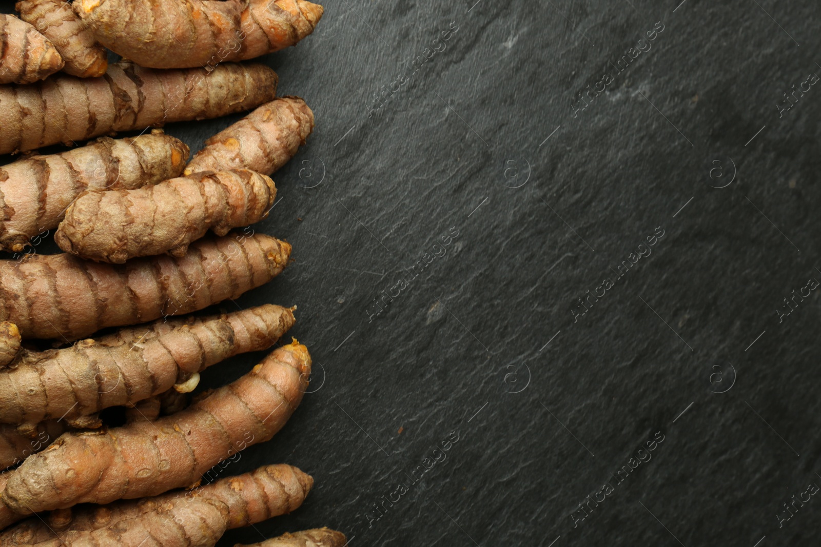 Photo of Many raw turmeric roots on black textured table, flat lay. Space for text