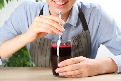 Photo of Woman with glass of fresh beet juice at wooden table, closeup