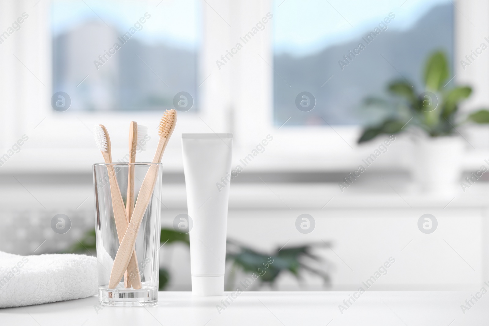 Photo of Bamboo toothbrushes in holder, toothpaste and towel on white table indoors. Space for text