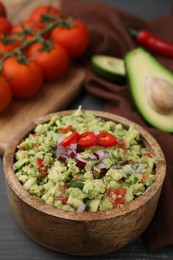 Photo of Bowl of delicious guacamole and ingredients on grey wooden table, closeup