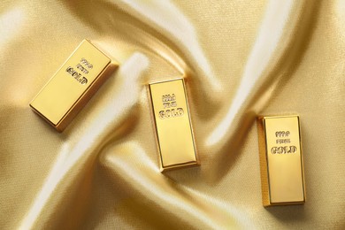 Photo of Gold bars on shiny silk fabric, flat lay