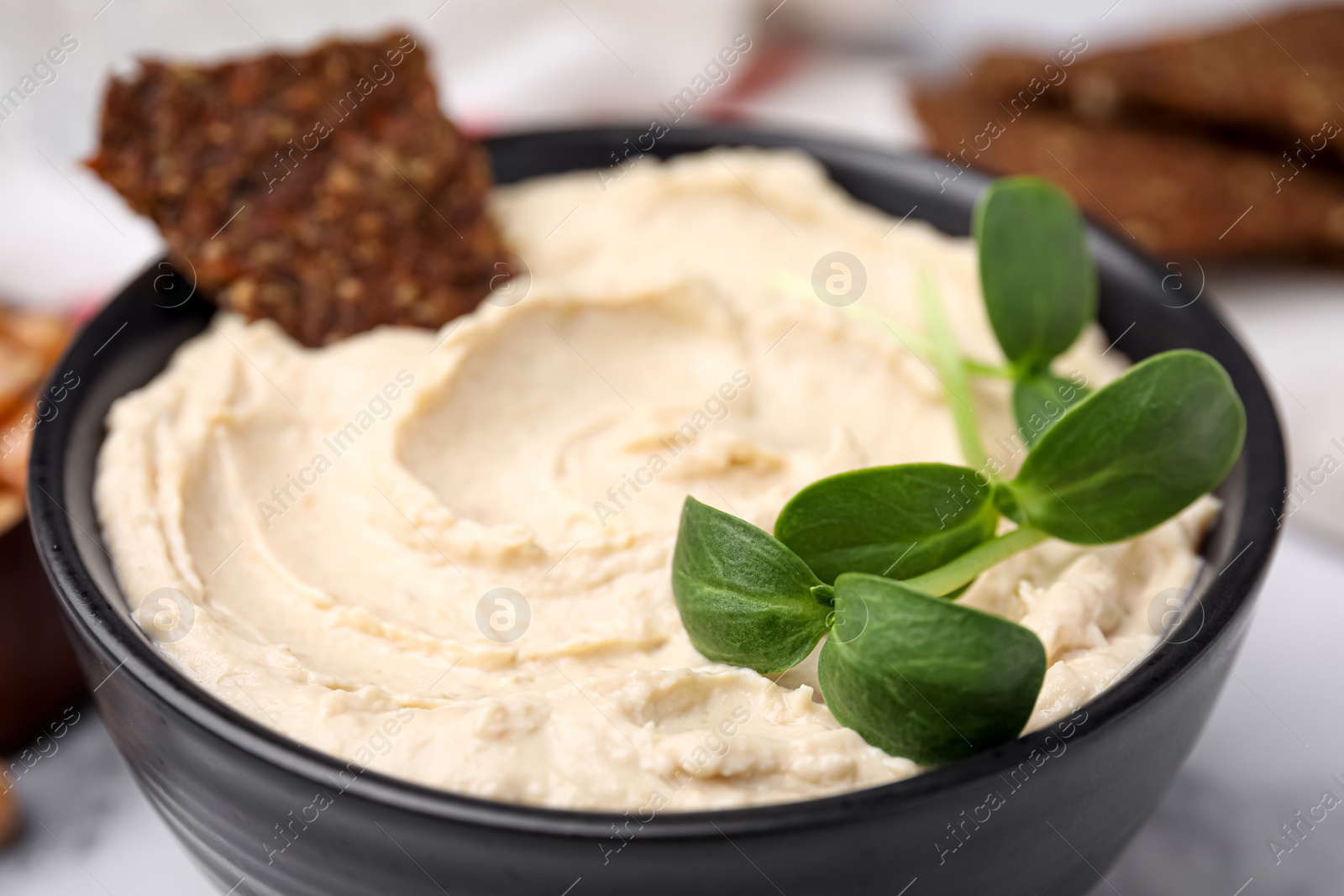 Photo of Bowl of delicious hummus with crispbread, closeup