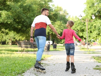 Photo of Father and son roller skating in summer park, back view