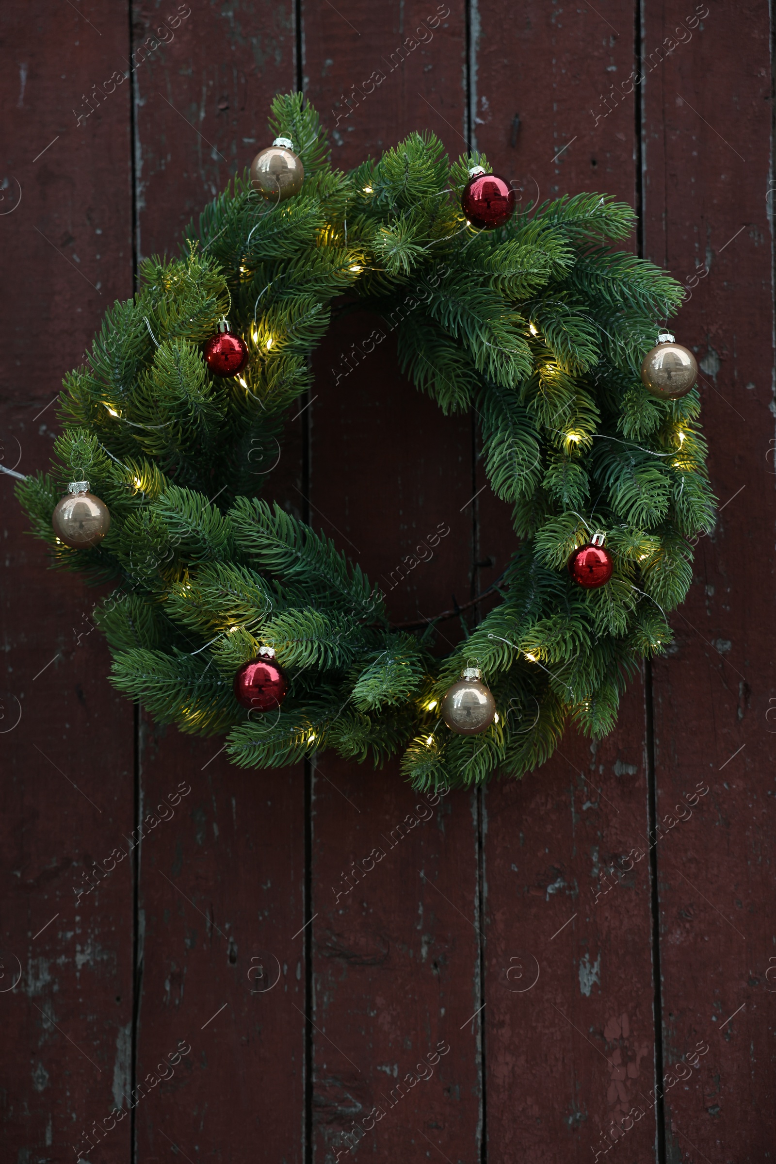 Photo of Beautiful Christmas wreath with baubles and string lights hanging on brown wooden wall