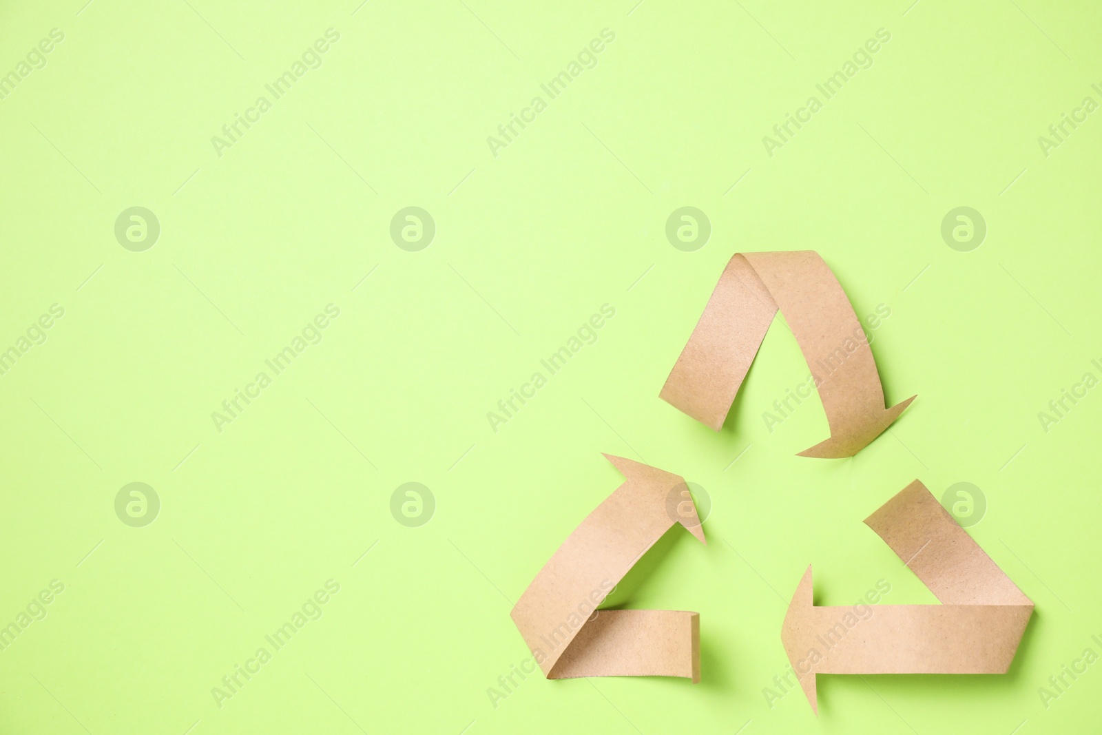 Photo of Recycling symbol cut out of paper on green background, top view. Space for text